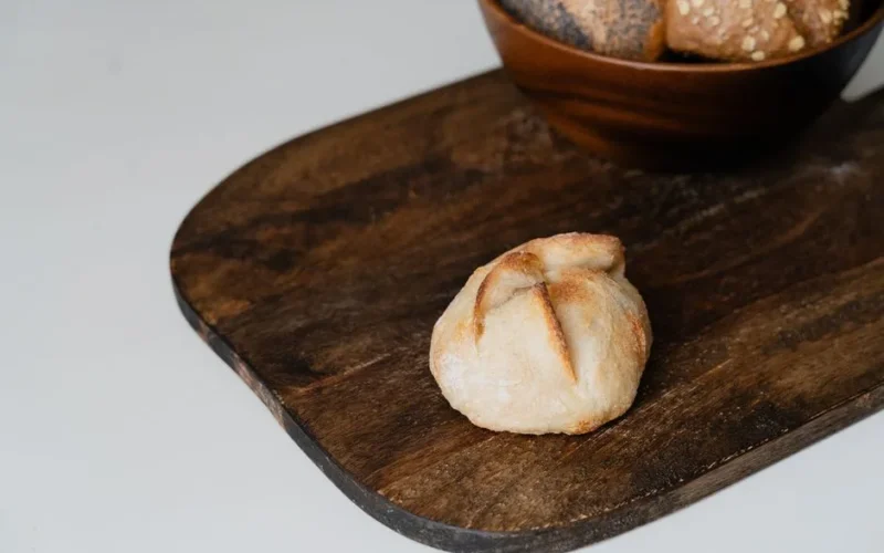 Close-up of a single artisan bread roll on a rustic wooden board, highlighting homemade bakery goods.