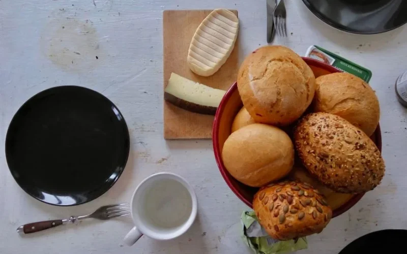 A cozy breakfast setting with assorted rolls and cheese on a wooden board.