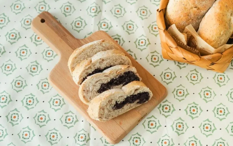 A delicious variety of bread slices on a wooden cutting board beside a wicker basket of buns.