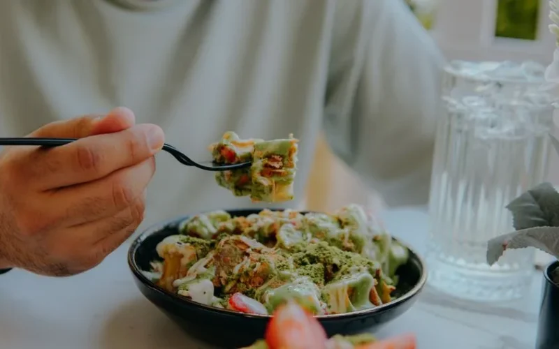 Close-up of a person eating creamy green sauce pasta at a table