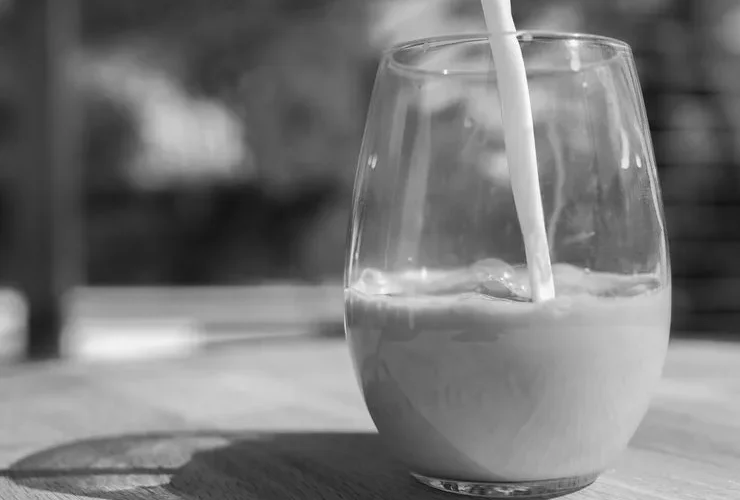 Artistic black and white photo of milk gracefully pouring into a glass on a wooden table.