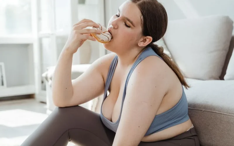 A woman in activewear relishes a donut while sitting indoors, embracing relaxation.