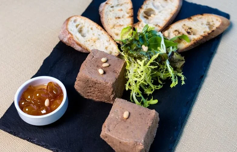Delicious liver pâté with toasted baguette, salad, and chutney on a slate serving board.