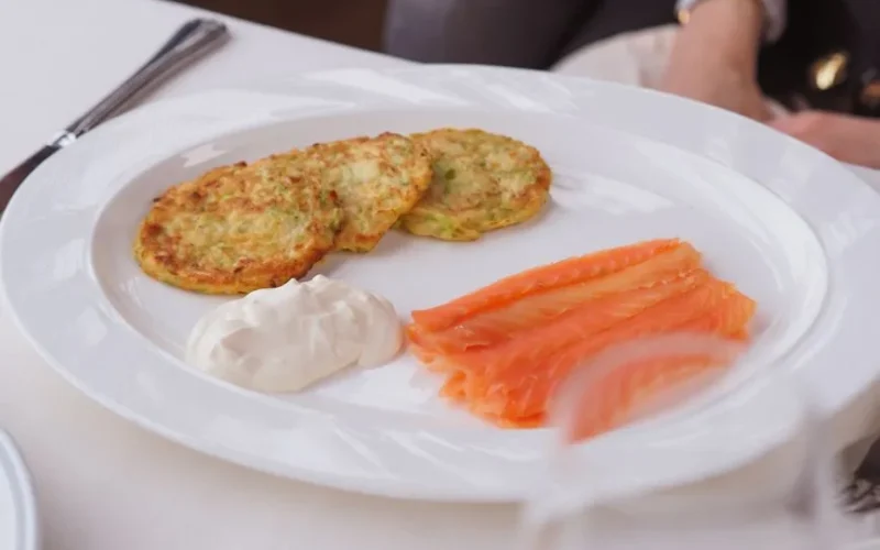 Delicious salmon slices with crispy potato pancakes and creamy sauce on a white plate.