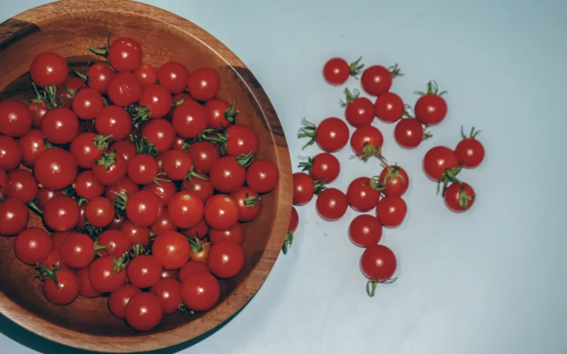Step into a world where vibrant flavors meet artistic finesse with this exquisite top view still-life photograph by Raju C Reddy. In the spotlight is a rustic wooden bowl, lovingly cradling a bountiful collection of fresh red cherry tomatoes. Each tomato is a miniature masterpiece, a burst of crimson against the rich wooden canvas, invoking a sense of rustic charm and wholesome indulgence. Set against a serene light blue background, a few stray cherry tomatoes playfully scattered like droplets of inspiration complete the composition, adding depth and balance to the visual tapestry. "Cherry Tomatoes Serenade" captures the essence of nature's bounty and creative vision in perfect harmony, an ode to the simple pleasures that color our lives.