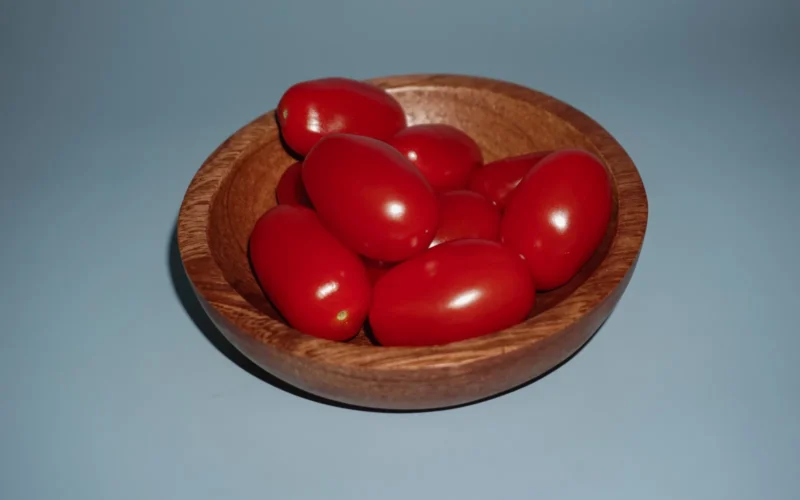 Raju C Reddy's still-life photograph, "Elegant Essence," encapsulates the graceful allure of the Red-Juliet tomato. Against a serene light blue background, a rustic wooden bowl cradles the singular beauty of this exquisite tomato variety. The tomato rests as a centerpiece, its rich red hue standing out against the soft backdrop. The careful interplay of light and shadow highlights the tomato's smooth skin and inviting curves. "Elegant Essence" captures the essence of this delicacy, inviting you to admire not just its color and form, but to also anticipate the sumptuous flavors that lie within this petite treasure.