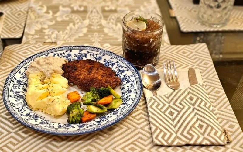 Tasty dinner setting featuring mashed potatoes, breaded cutlet, vegetables, and a cold drink.