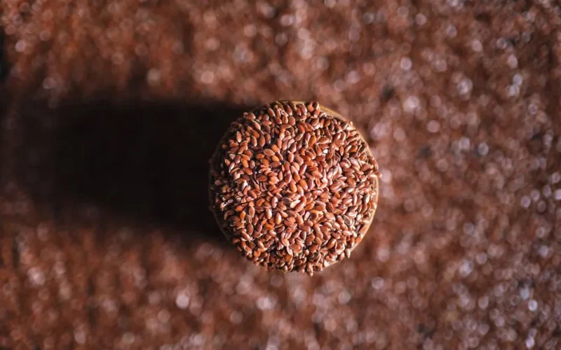 A top-down view of a jar filled with flax seeds, surrounded by scattered seeds on the surface.