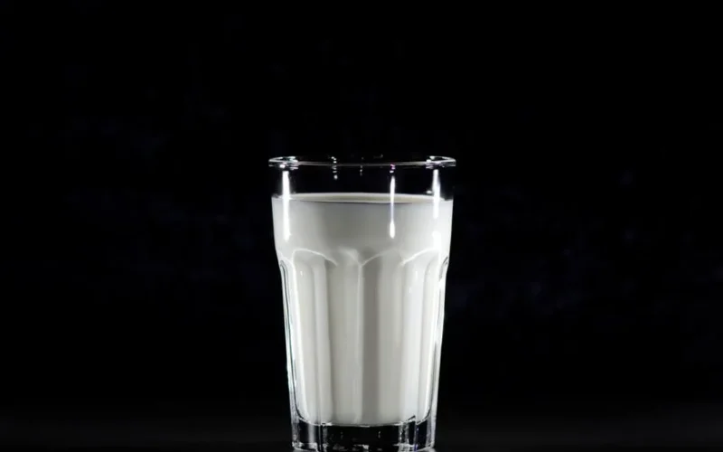A glass of fresh milk against a black background, emphasizing simplicity and nutrition.