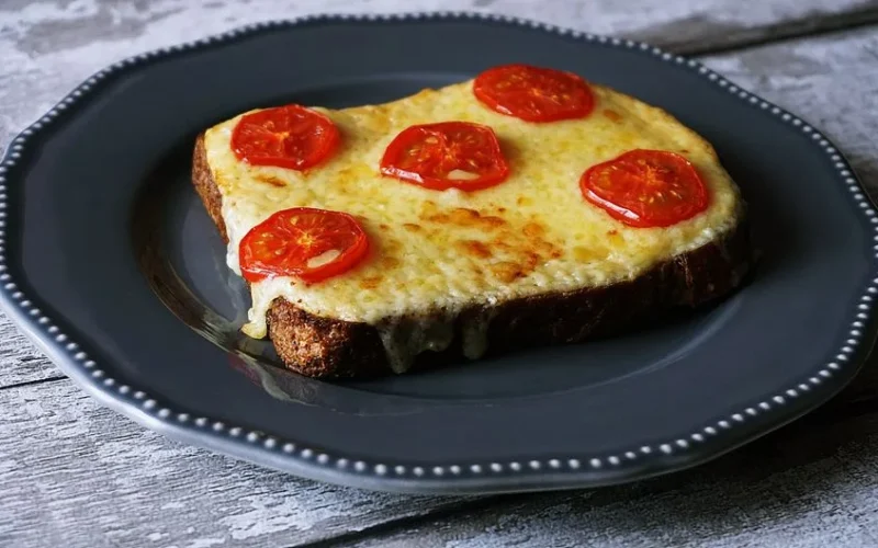 Delicious melted cheese and tomato toast on a rustic grey plate, perfect for breakfast or snack.
