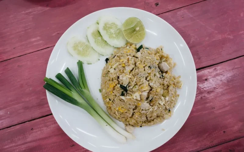 Asian fried rice served on a white plate with cucumbers, lime, and green onions.