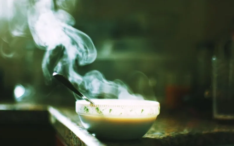 A steaming bowl of soup sits on a kitchen counter, emitting warm wafts into the air.