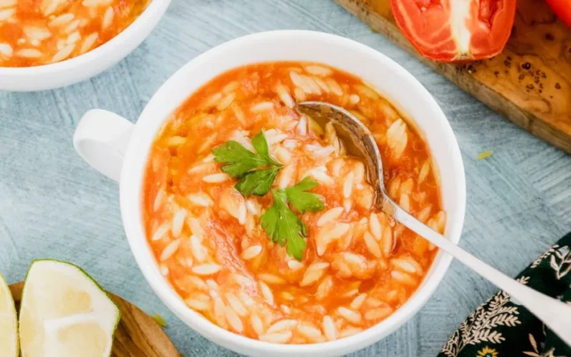 A close-up of flavorful orzo soup garnished with cilantro and lime wedges.