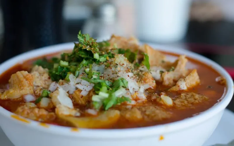 Close-up of a delicious Mexican menudo soup garnished with fresh herbs in a white bowl.