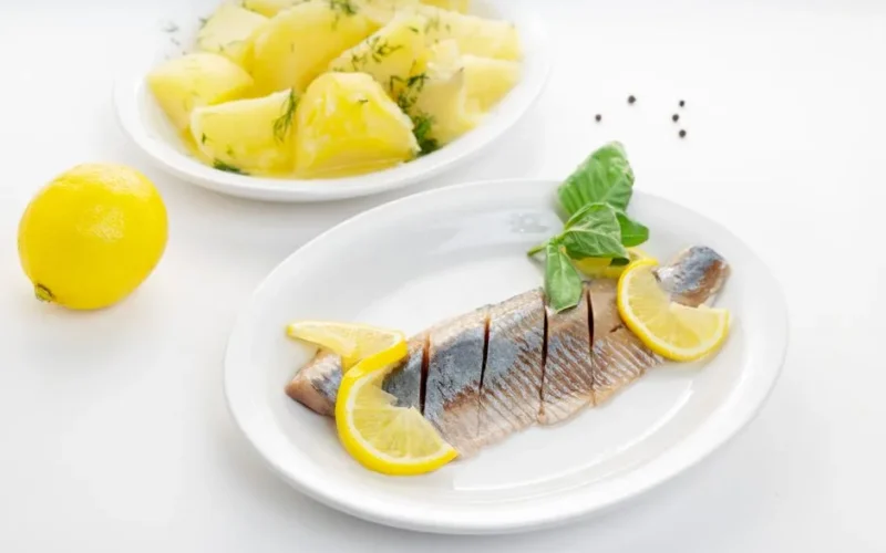 Delicious fish fillet with lemon slices and herb potatoes on white plates.