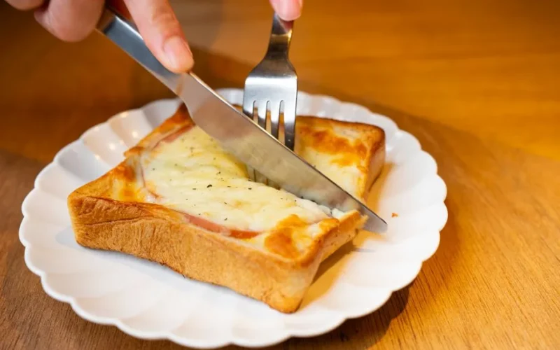 Close-up of a grilled cheese toastie being cut open, served on a white plate in Tokyo.