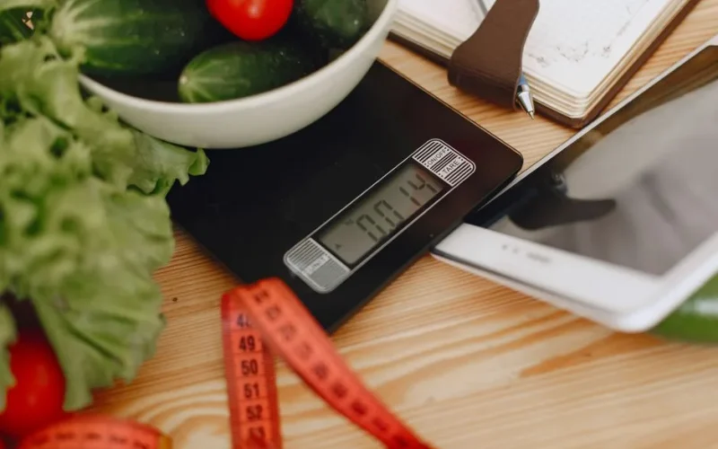 A bowl of fresh vegetables on a kitchen scale with measurement tools, depicting a healthy lifestyle.