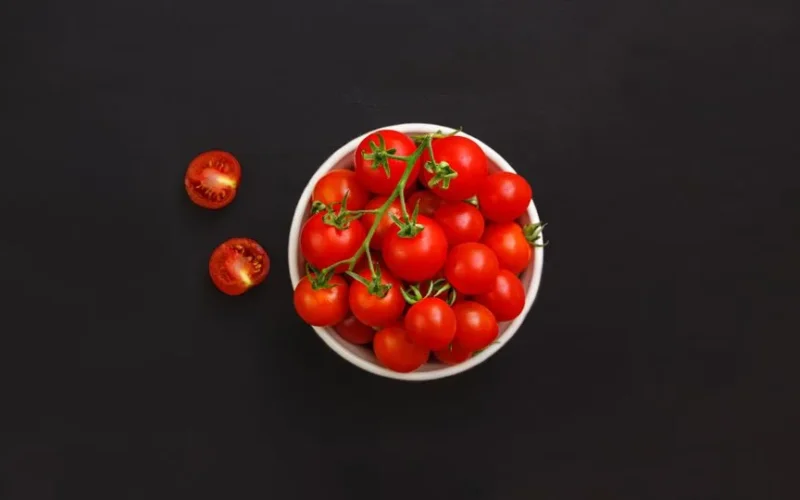 Top view of fresh red healthy tomatoes with green stems placed on black background