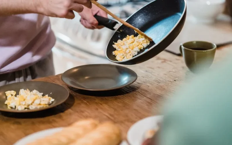 A man serves freshly made scrambled eggs onto a plate in a cozy kitchen setting.