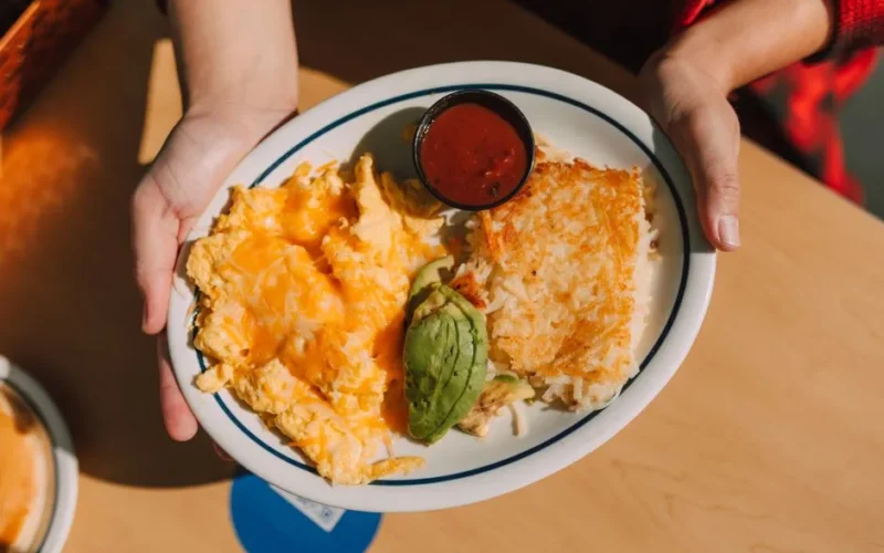 Plate of cheesy scrambled eggs, avocado, hash browns, and sauce, perfect for breakfast.