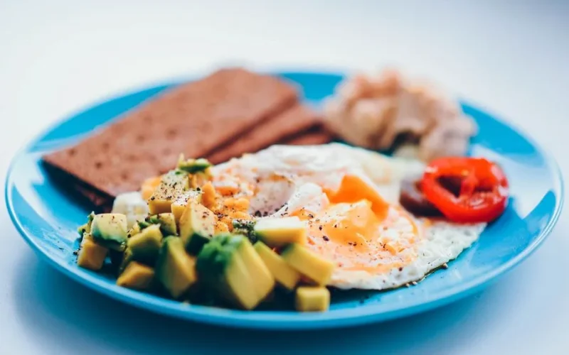 Bright and colorful breakfast featuring fried eggs, avocado, and fresh vegetables on a blue plate.