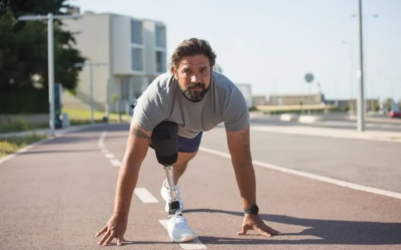 A determined man with a prosthetic leg prepares to run on an urban track, showcasing resilience.