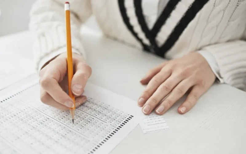 A student writing answers on a multiple-choice exam sheet at a desk.