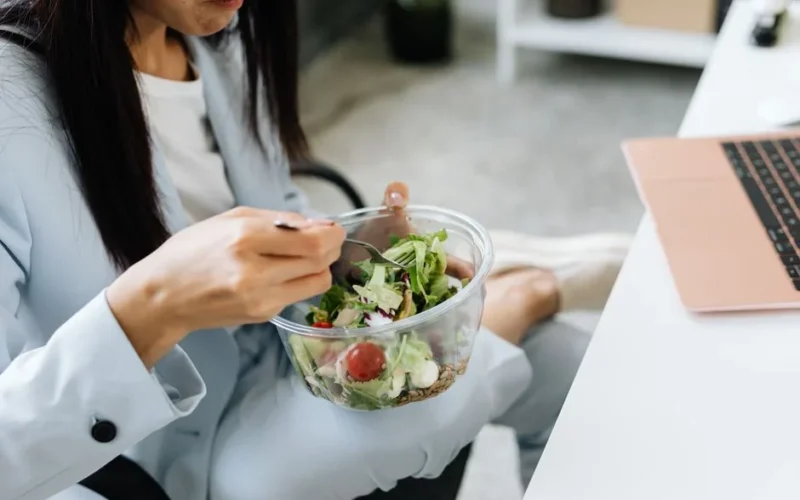 Adult woman eating a vegetable salad at her office desk, embodying healthy lunchtime habits.