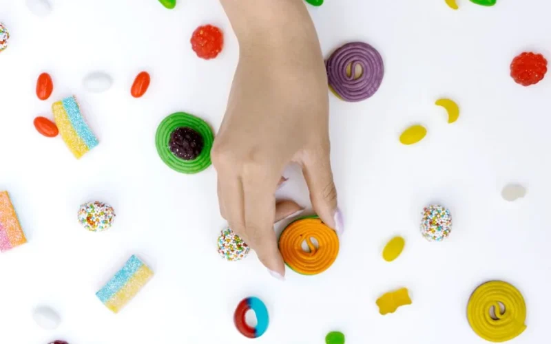 Top view of a hand holding assorted colorful candies on a white background.