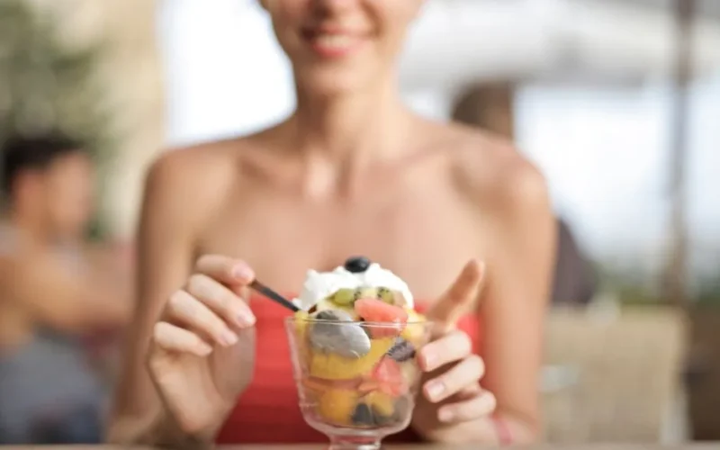 Happy woman eating fruit salad at a cafe, enjoying a refreshing dessert.