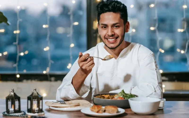 A smiling man enjoys a traditional meal indoors, surrounded by string lights.
