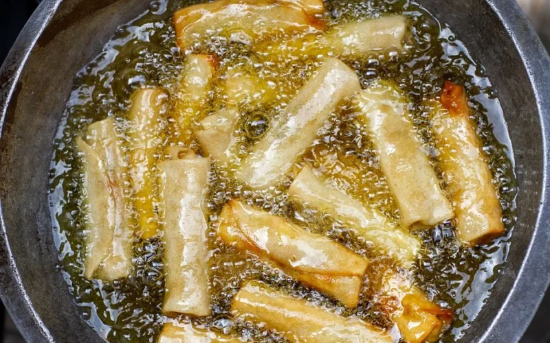 Close-up of golden spring rolls frying in hot oil, showcasing delicious texture and crispy edges.