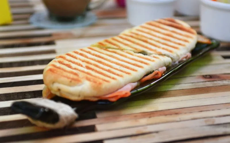 Tasty grilled panini sandwich with ham and cheese on a wooden table.