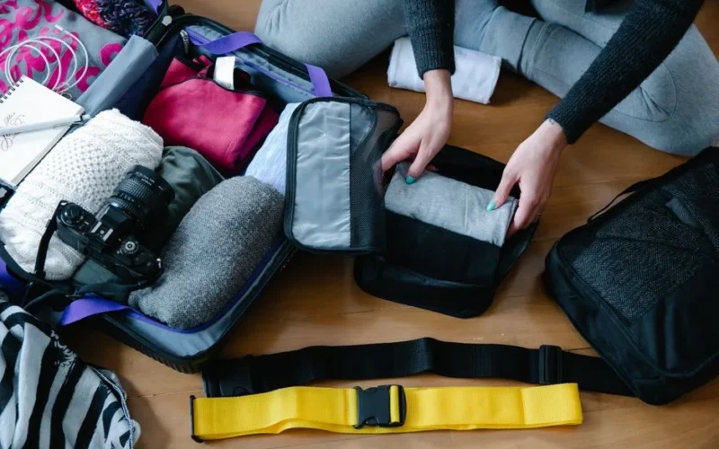 A woman arranging clothes and accessories into a suitcase, preparing for travel.