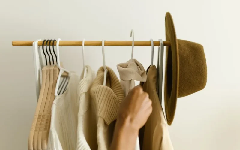 Stylish beige and brown clothes on a rack with a hand reaching in.