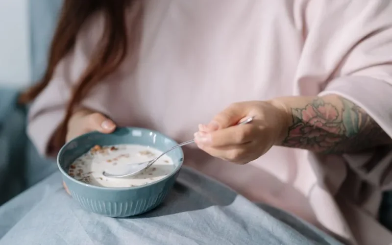 A woman with a tattoo enjoying a bowl of cereal with milk in a relaxed indoor setting.