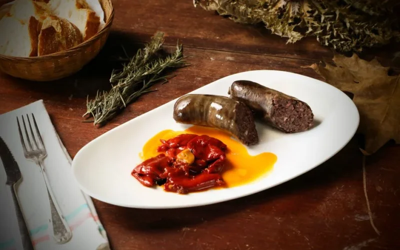 A rustic presentation of blood sausage with roasted red peppers and bread on a wooden table.