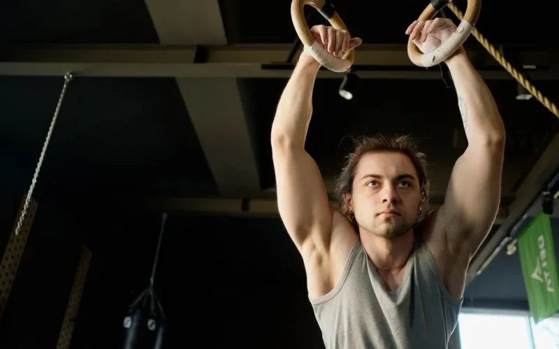 Focused young man exercising on gymnastic rings in a modern gym setting.