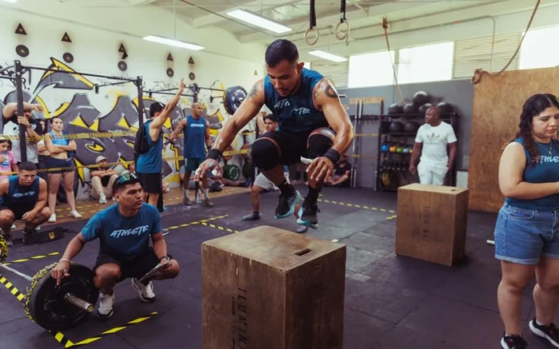 A lively gym scene in Pereira, Colombia, featuring a power box jump challenge with diverse participants.