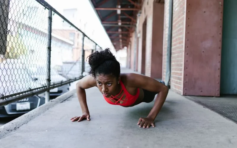 Focused woman in activewear doing push-ups outdoors against a brick wall.