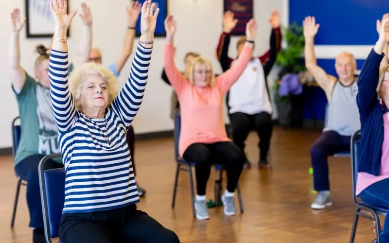 Group of senior adults participating in a chair exercise class, promoting fitness and healthy lifestyle.