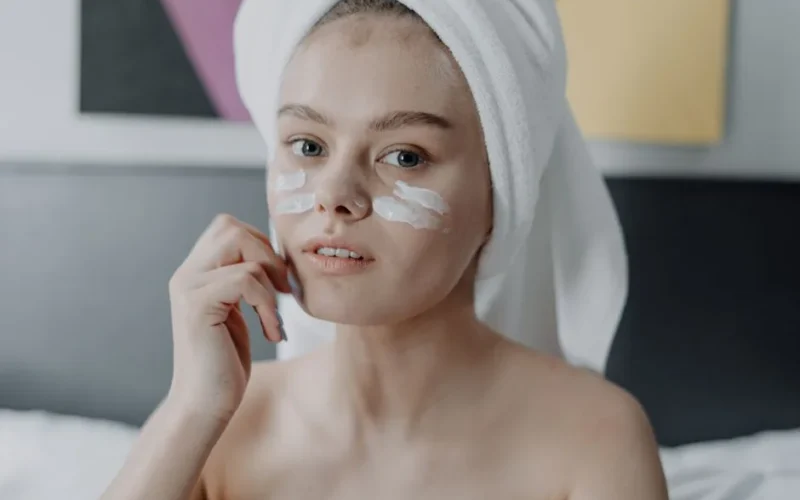 A young woman with facial cream and a towel wrapped on her head, focused on skincare.