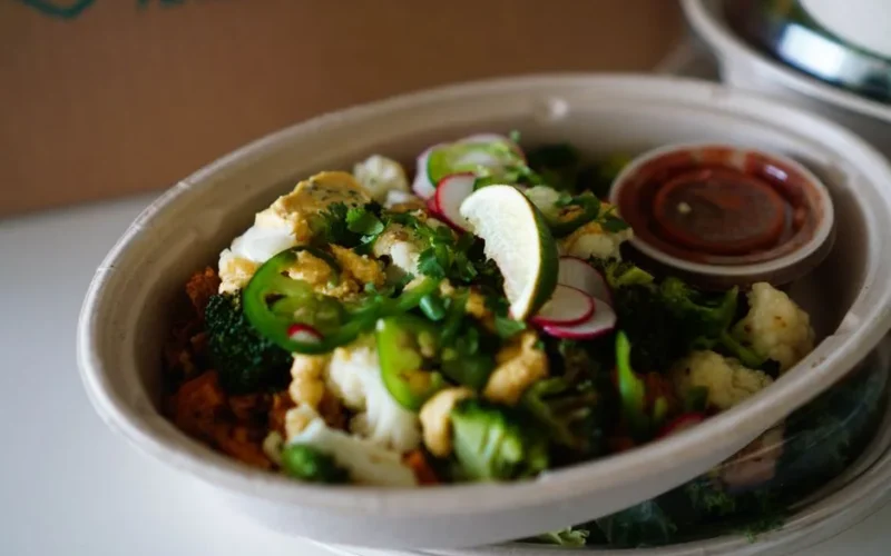 Colorful vegetable salad bowl with broccoli, cauliflower, jalapeno, and lime in eco-friendly packaging.