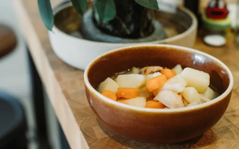 Close-up of a steaming vegetable stew served in a rustic ceramic bowl on a wooden table.