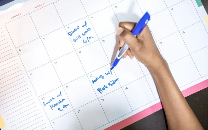 Person writing appointments on a calendar with a blue pen. High angle view.