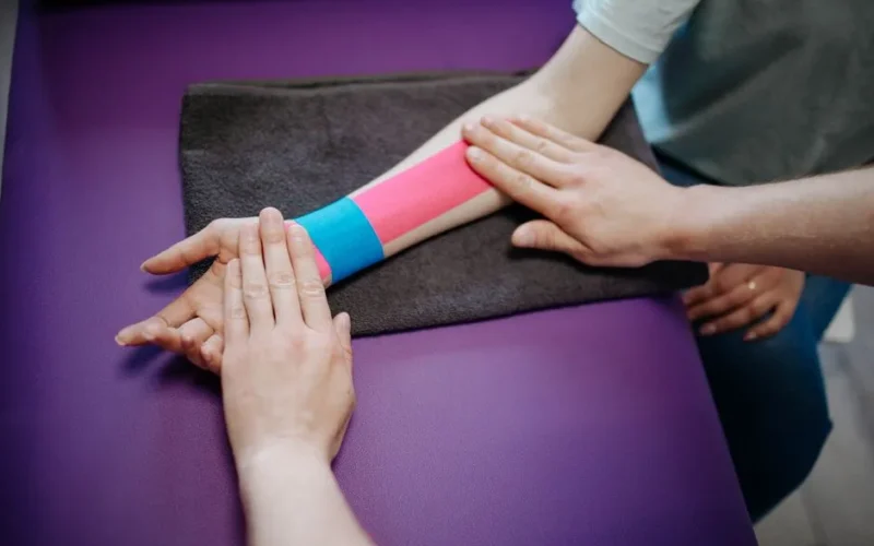 A therapist carefully applying colorful kinesiology tape on a patient's forearm for supportive therapy.