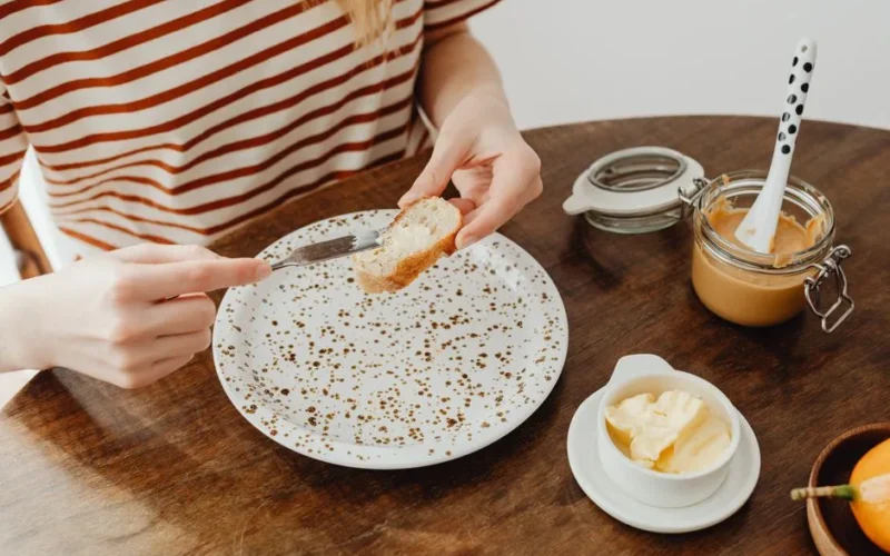 Close-up of person spreading peanut butter on bread slice at table.