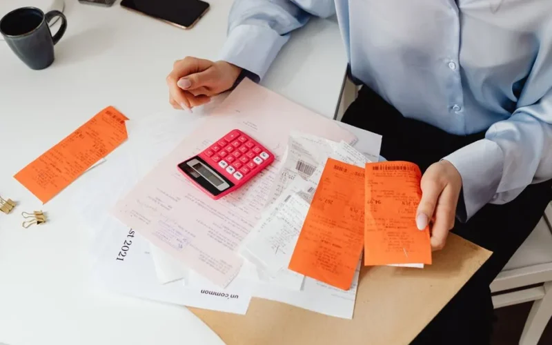 A woman reviews receipts and calculates expenses at a desk with a pink calculator.