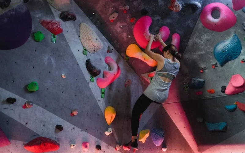 Back view of anonymous female athlete climbing on boulders in professional gym for mountaineering training