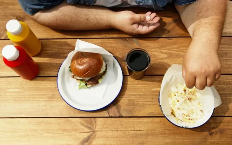 Overhead shot of a meal with burger, fries, condiments, and a drink on a wooden table.